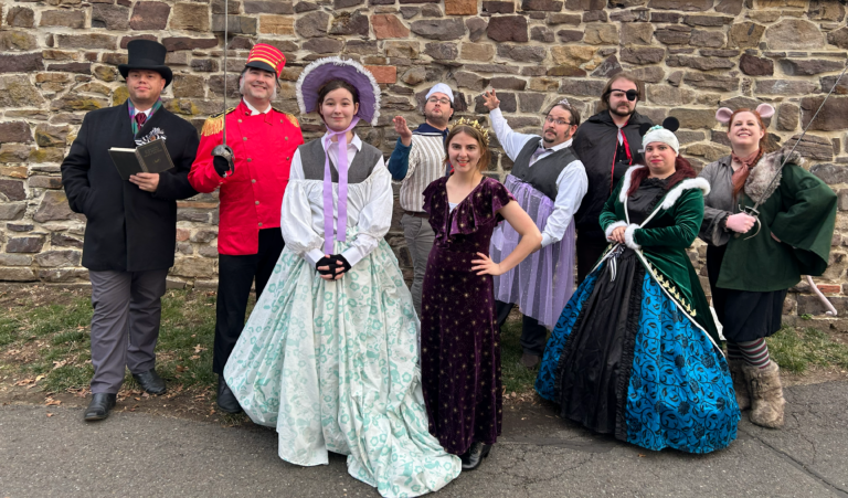 A photograph of a group of nine people dressed in festive Victorian garb and costumes for The Nutcracker play